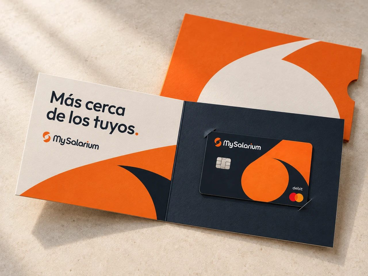 An open cream and navy MySalarium card folio with curved orange graphics, the message Más cerca de los tuyos, a debit card and a matching orange sleeve
